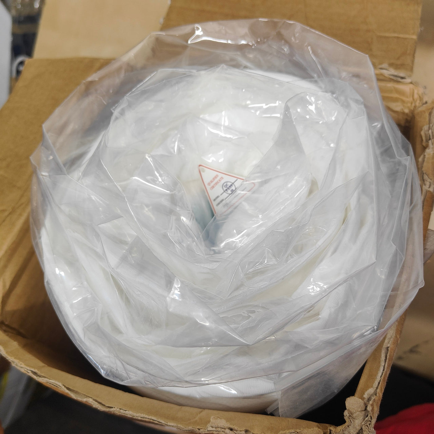 Roll of white paper or fabric in a clear plastic bag inside a cardboard box.