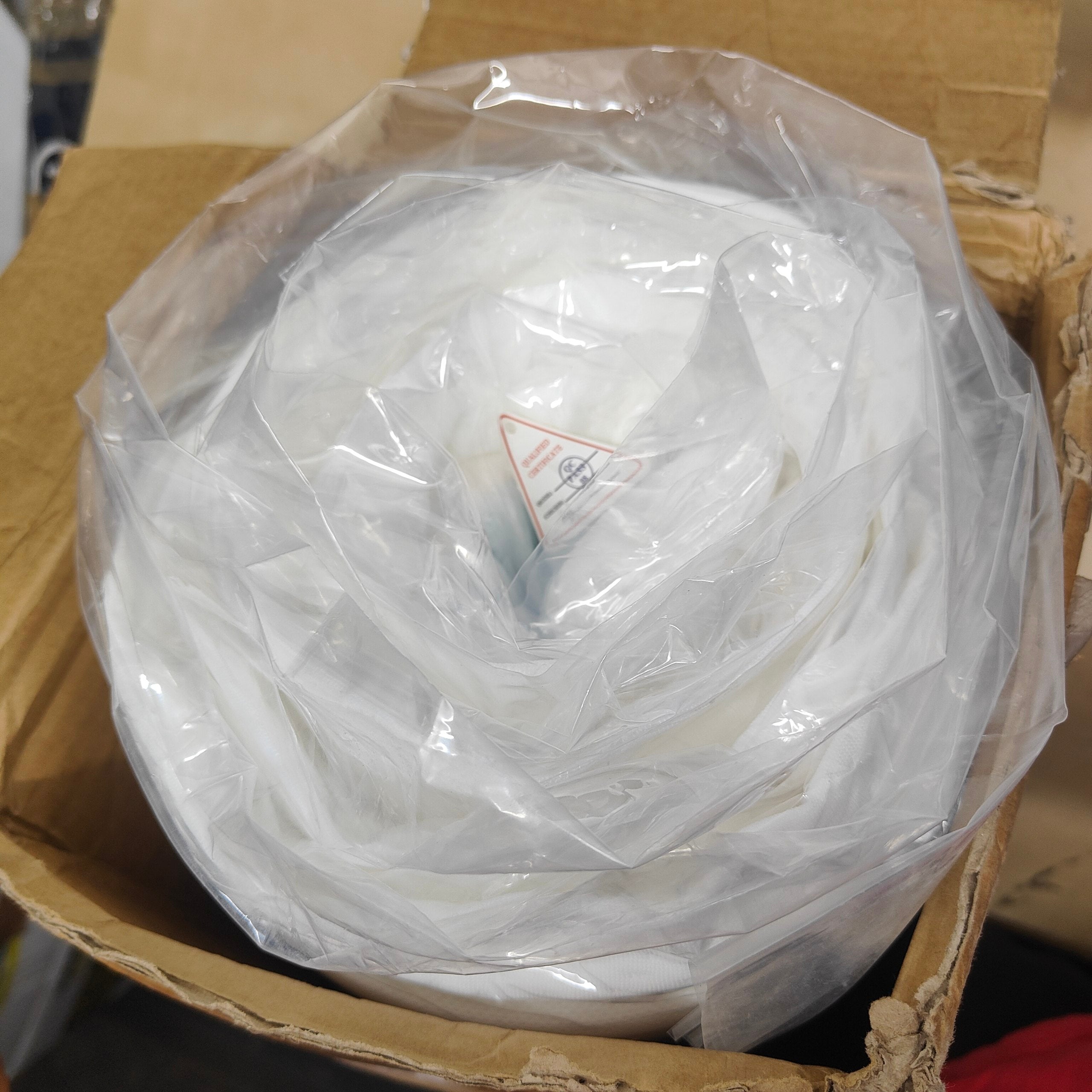 Roll of white paper or fabric in a clear plastic bag inside a cardboard box.
