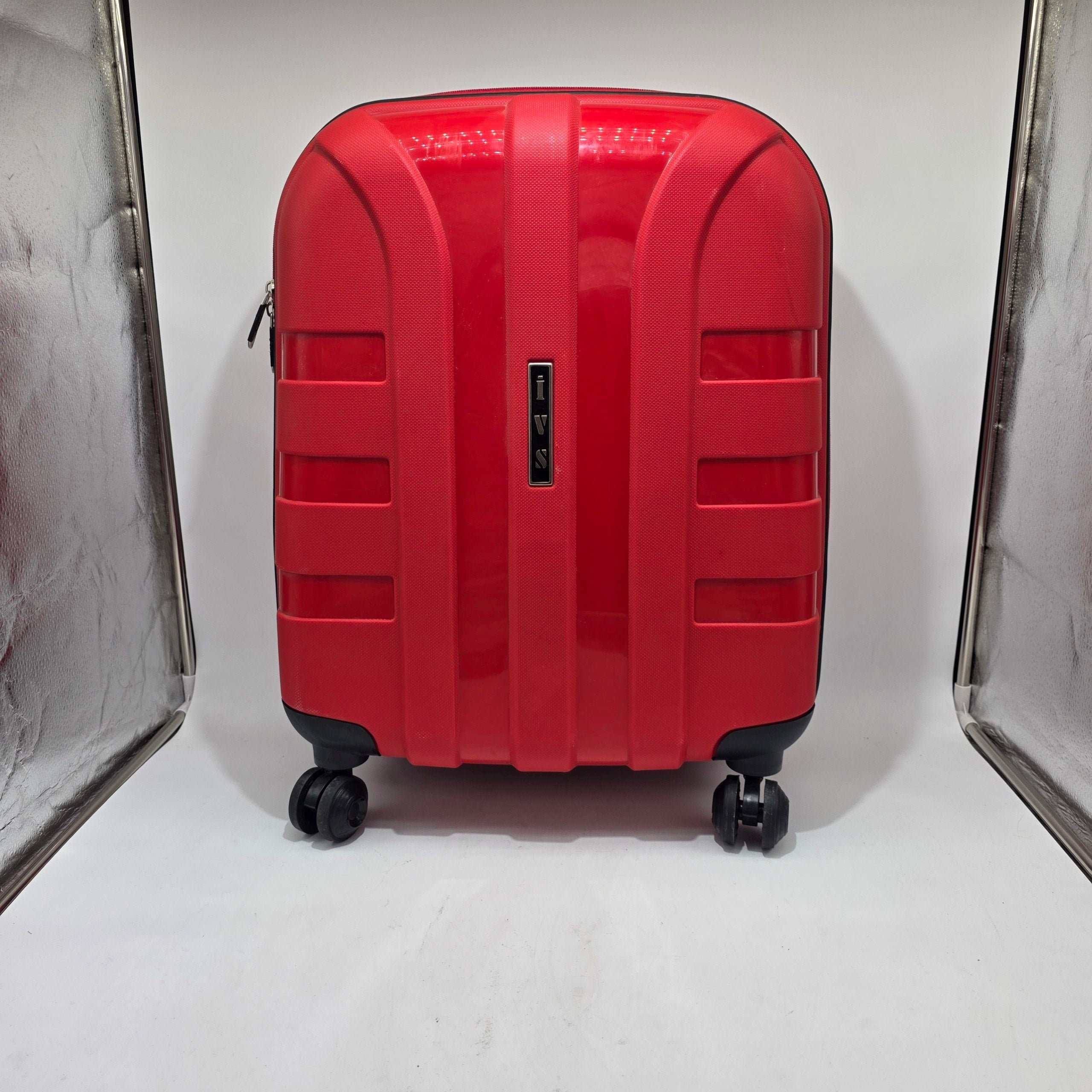 A bright red hard-shell spinner suitcase photographed from the back, standing upright on a white studio surface with reflective light boxes visible on both sides.