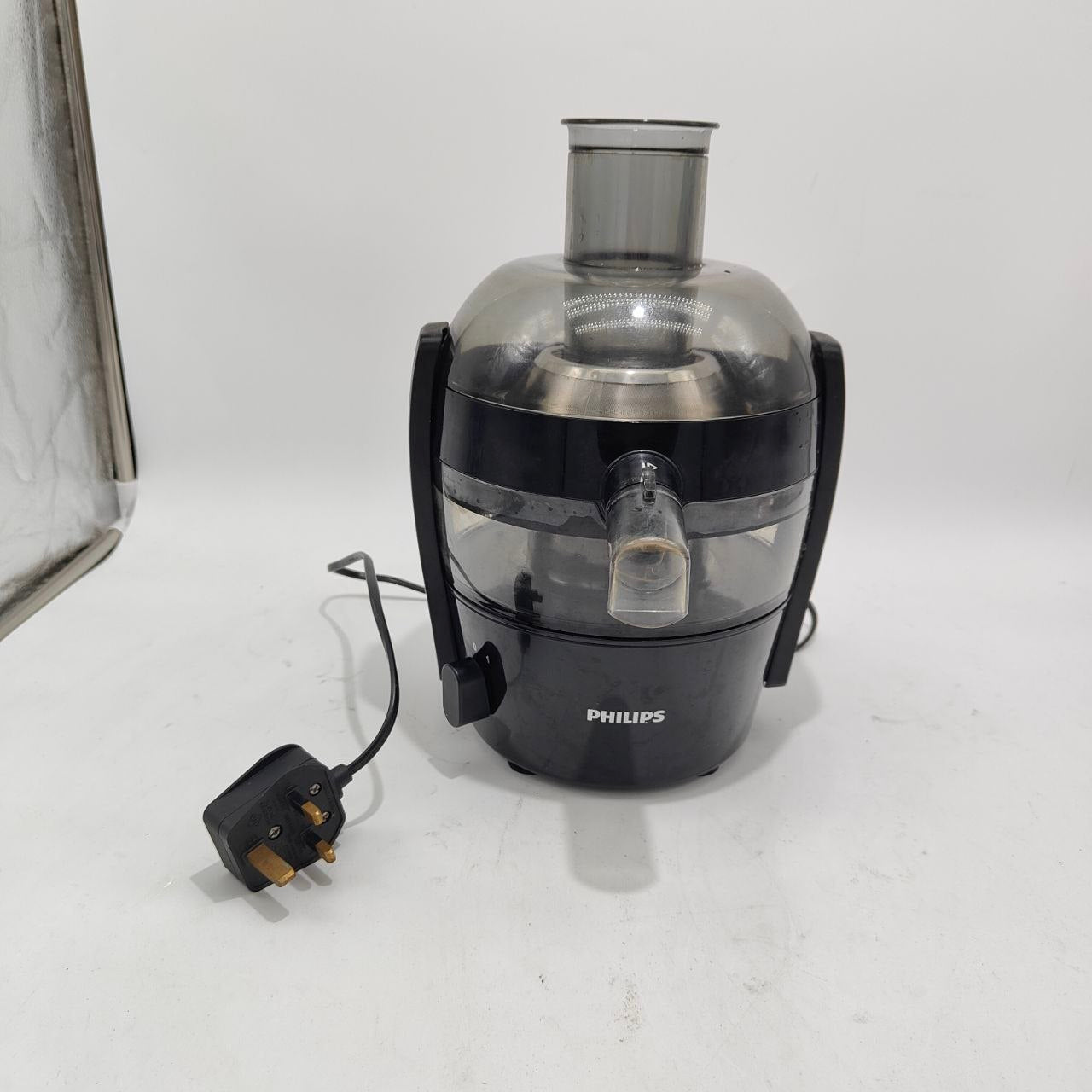 A Philips countertop juicer with a black plastic base and clear plastic hopper, shown with its power cord on a white surface.