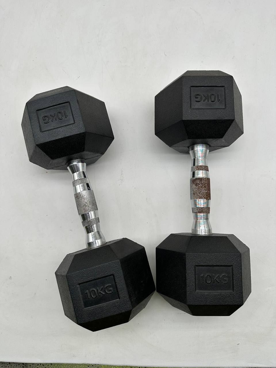 Two black 10kg hex dumbbells with silver metal handles, displayed side-by-side on a light gray surface.