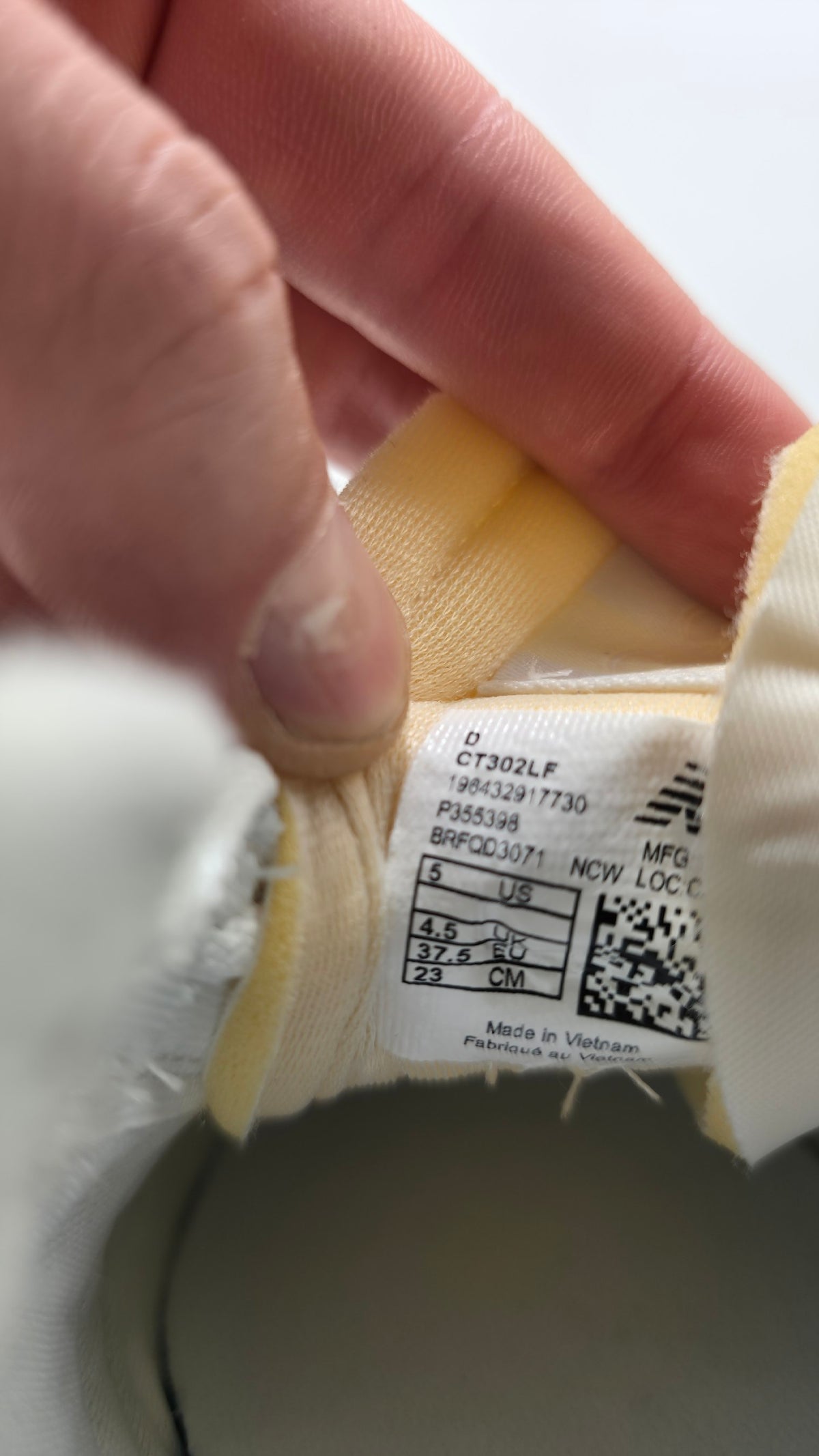 A close-up of a hand holding the interior collar of a white and yellow garment, showing the sewn-in size and care label.