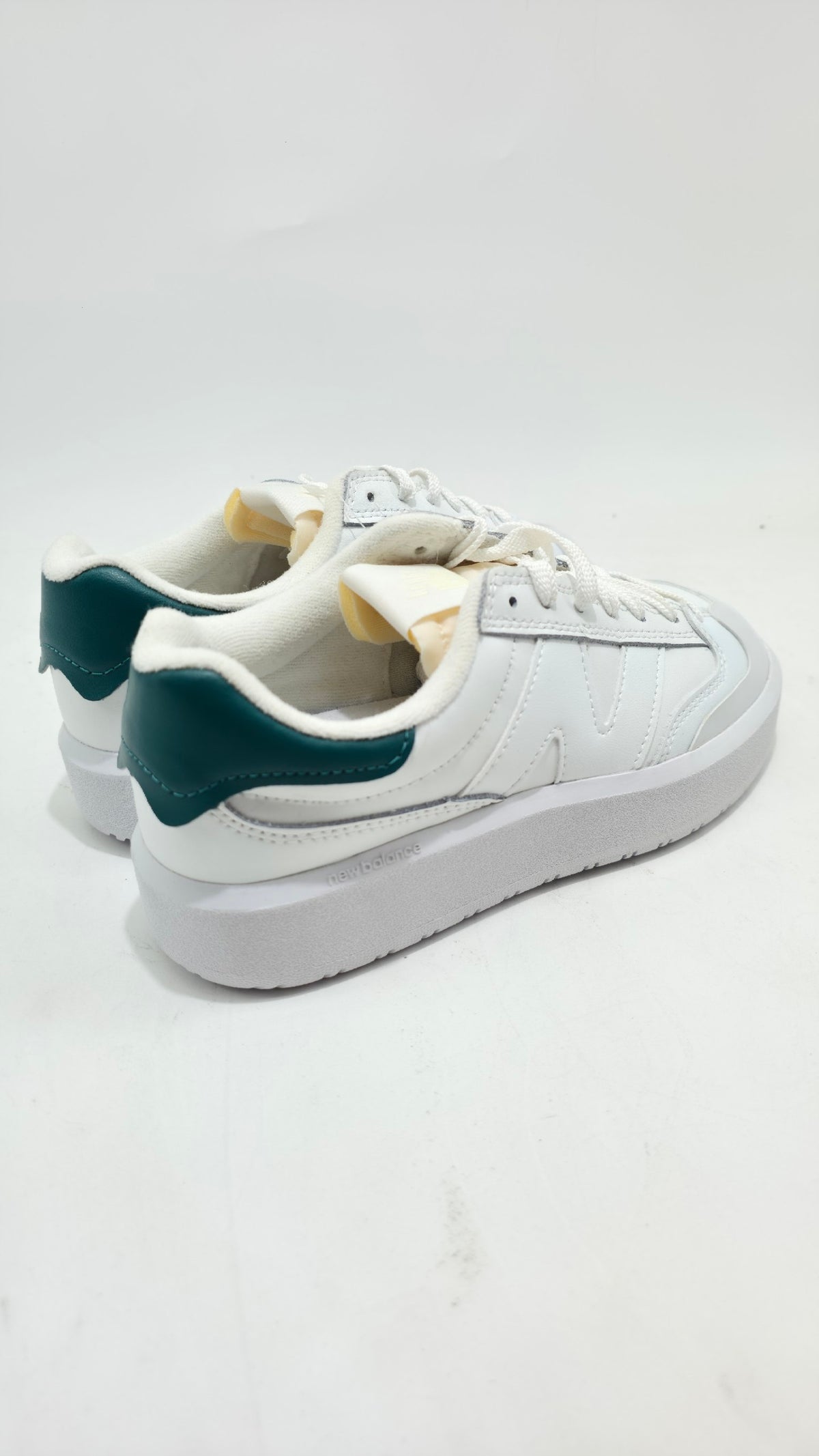 A pair of white low-top sneakers with dark green heel accents, shown from a side-rear angle on a plain white studio background.