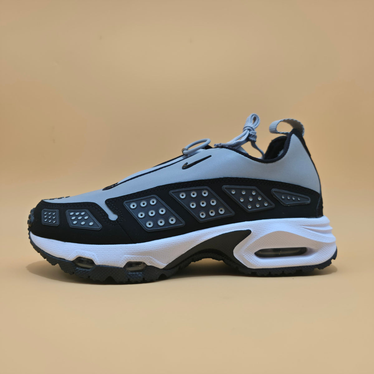 A Nike sneaker in light gray, black, and white, shown from the side profile against a solid beige background.