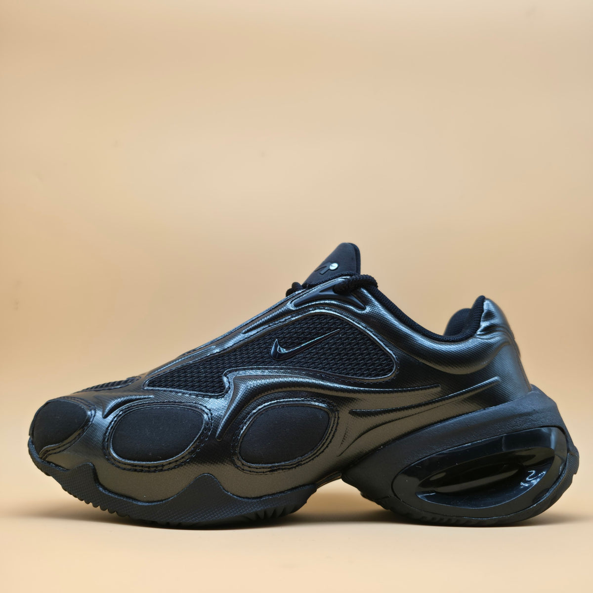 A dark navy blue Nike sneaker with a chunky, sculpted sole and glossy synthetic overlays, shown from a side profile against a solid beige background.