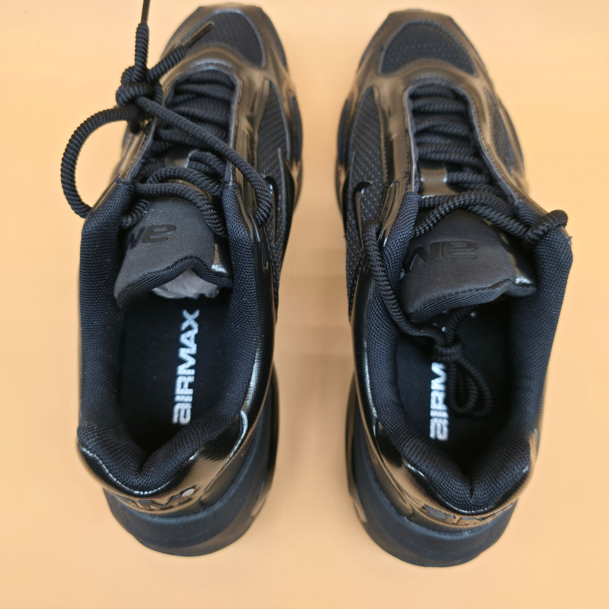 A pair of black Nike Airmax sneakers shown from a top-down view on a solid beige background.