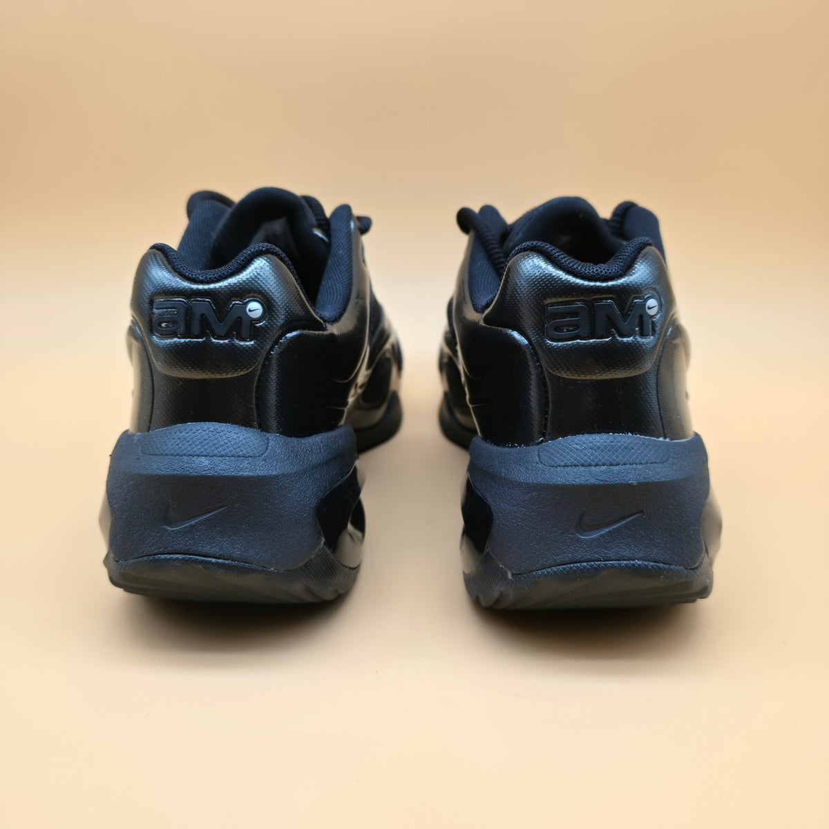 A pair of Nike Air Max 2013 sneakers in navy blue, shown from the back on a warm beige background.