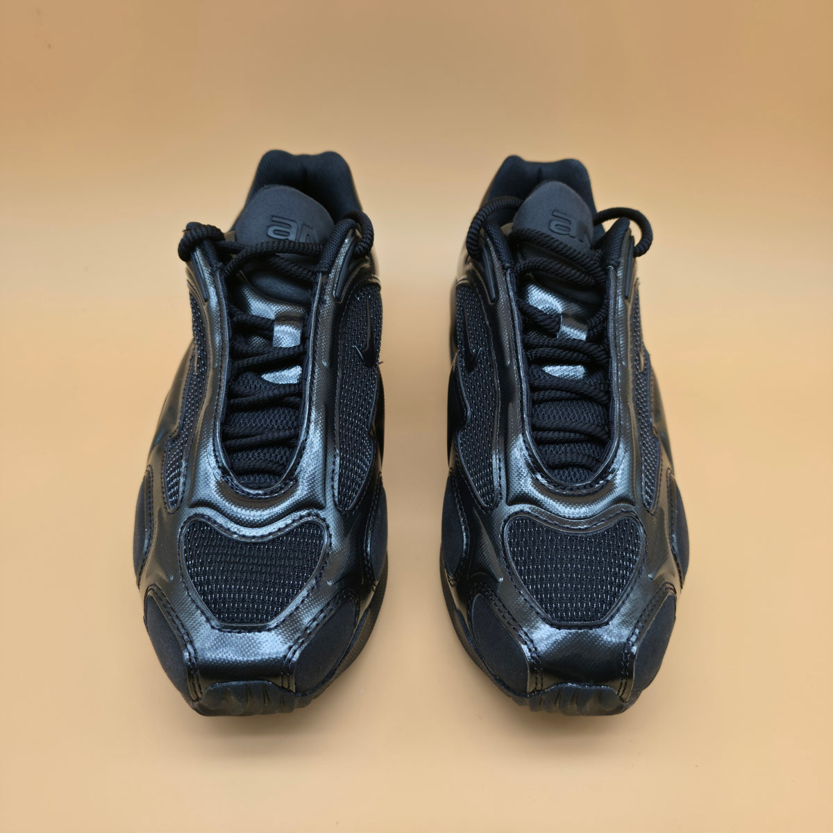 A pair of dark navy blue athletic sneakers with a glossy synthetic upper and mesh panels, shown from a front-facing perspective on a solid beige background.