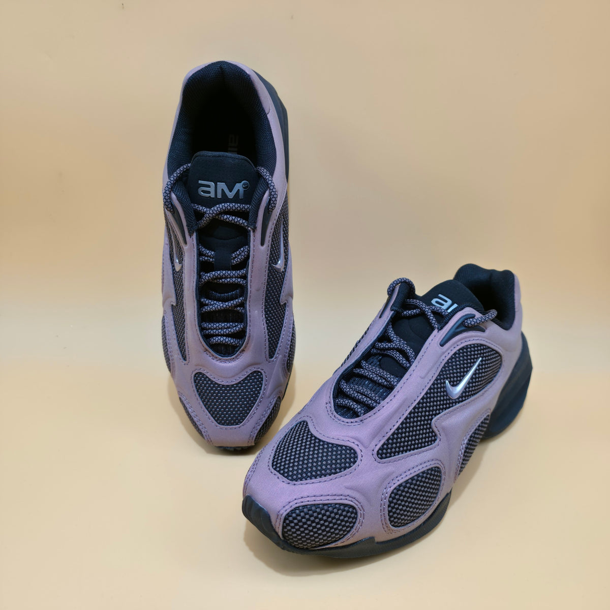 A pair of Nike Air Max 90 sneakers in a lavender purple and navy blue colorway, displayed on a plain beige background.