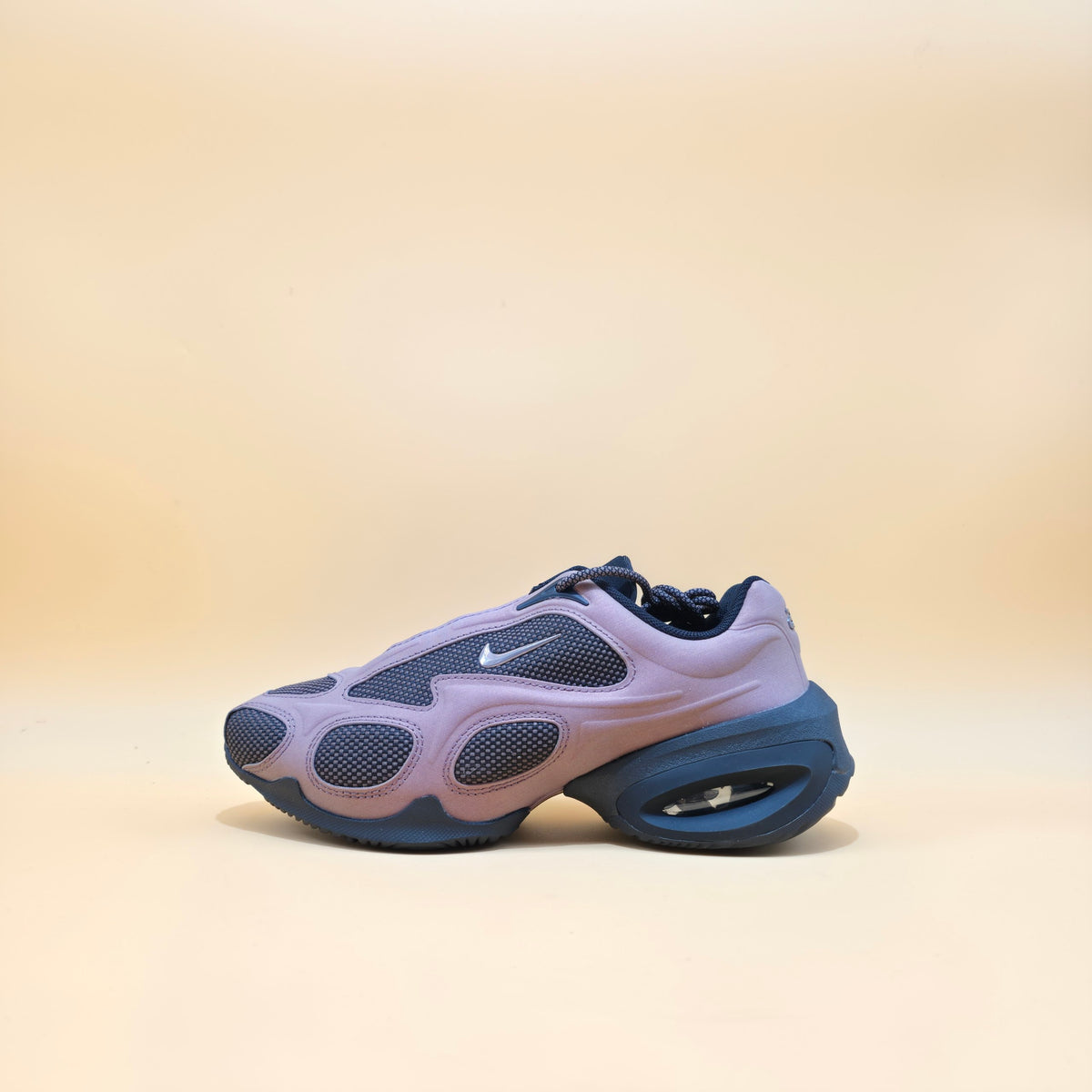 A Nike sneaker in a lavender and navy blue colorway, shown from a side profile against a warm beige background.