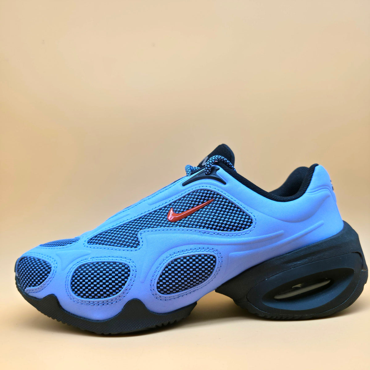 A Nike sneaker in vibrant blue and navy with a red Swoosh logo, shown from a side profile against a solid beige background.