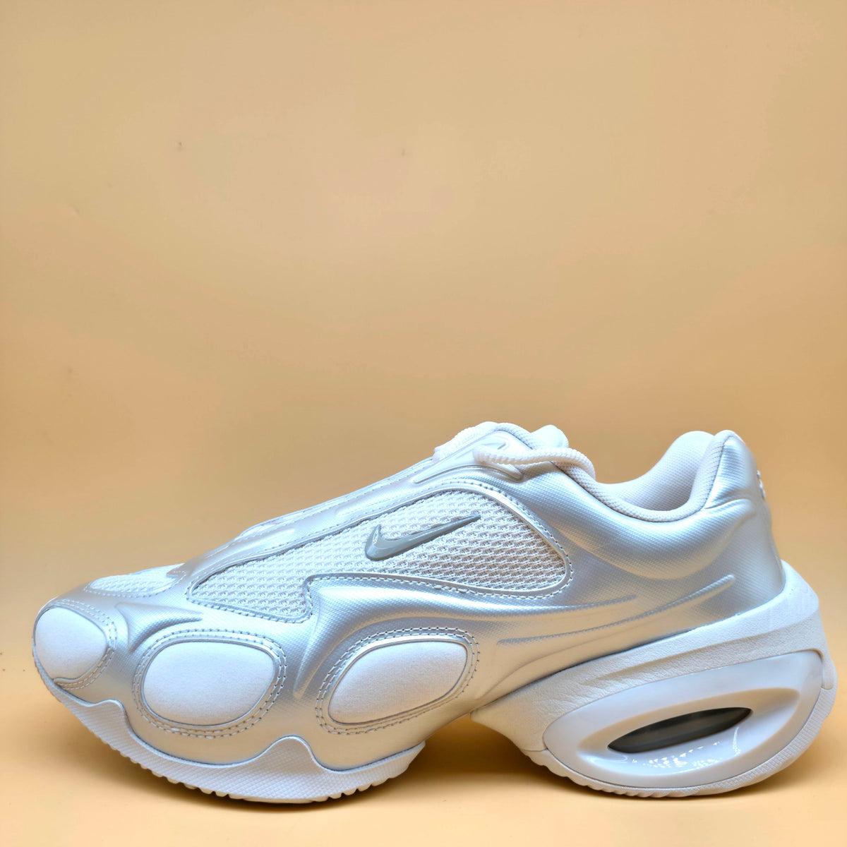A single Nike sneaker in metallic silver and white, shown from a side profile against a solid beige background.
