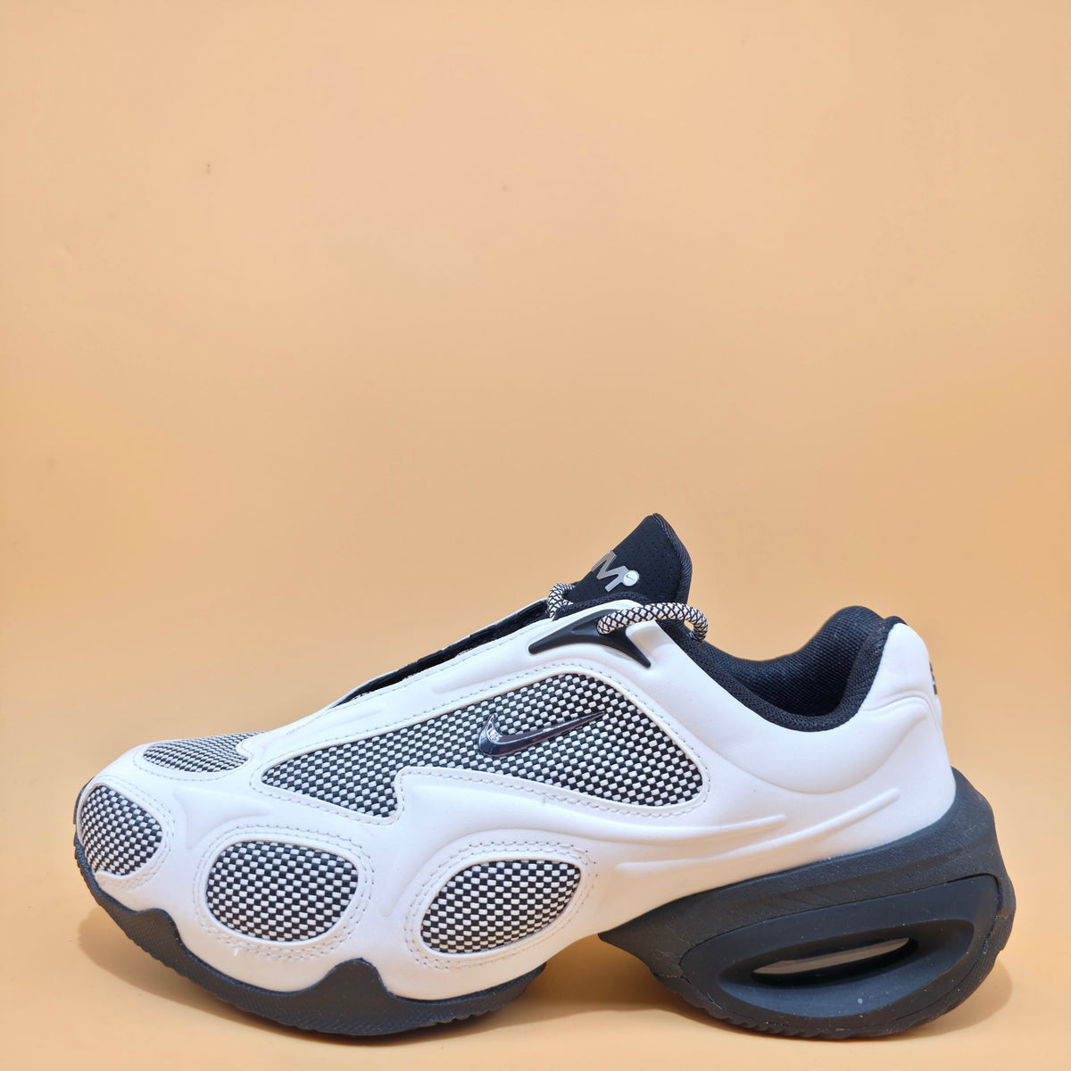 A white and navy blue Nike sneaker with a chunky sole and mesh panels, photographed on a solid beige background.