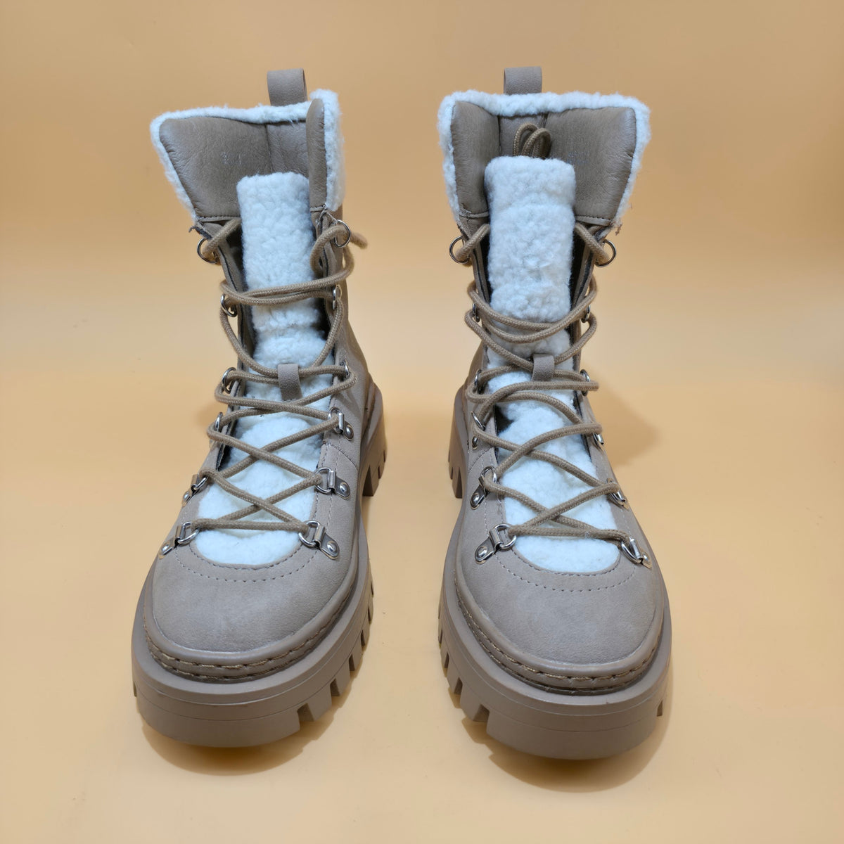 A pair of gray lace-up winter boots with light blue sherpa lining and chunky lug soles, shown against a solid beige background.