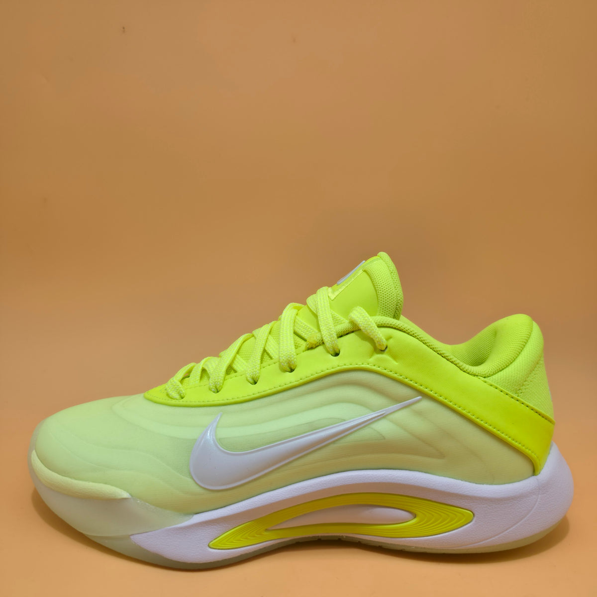 A Nike basketball shoe in neon yellow and light green with a white swoosh and white sole, photographed against a solid tan background.