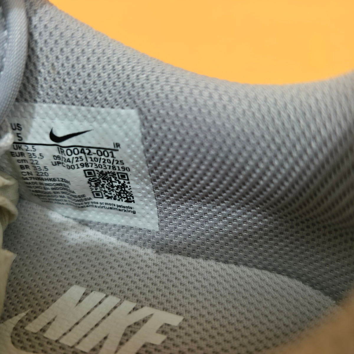 Close-up of a Nike shoe size and barcode label on the gray mesh insole of a sneaker, with a yellow-orange background visible above.