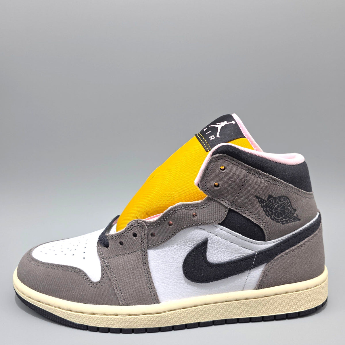 A high-top sneaker in gray suede and leather with white overlays, a black Swoosh and tongue, a bright yellow collar lining, and a cream midsole, photographed on a gray gradient background.