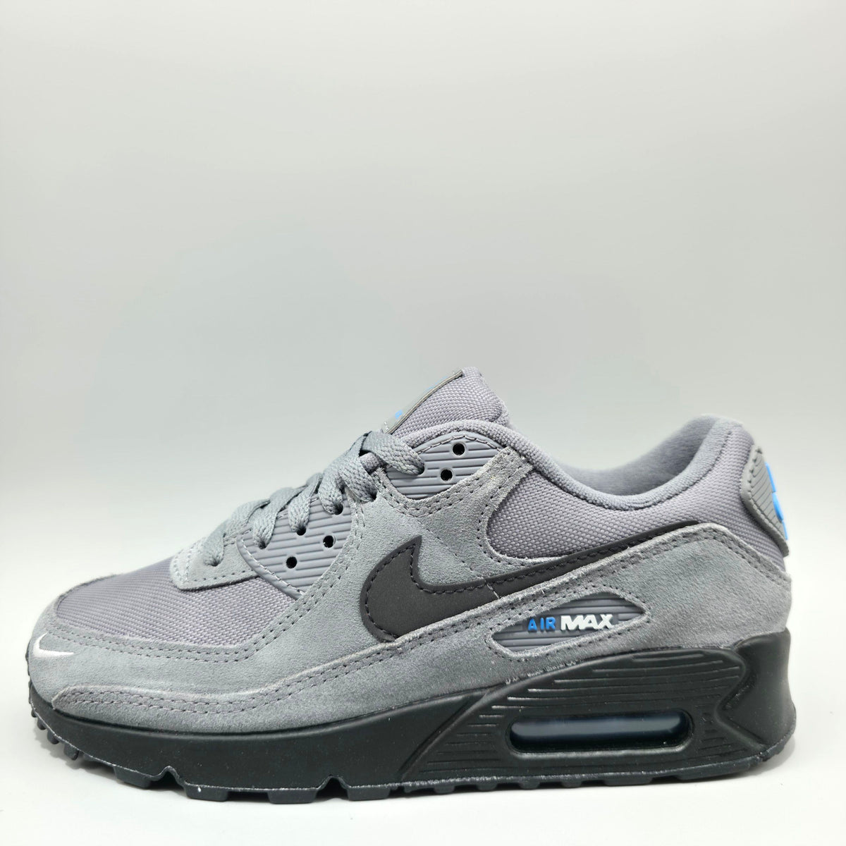 A Nike Air Max sneaker in gray suede and mesh with a dark gray Swoosh, a black sole, and a small blue accent on the heel.