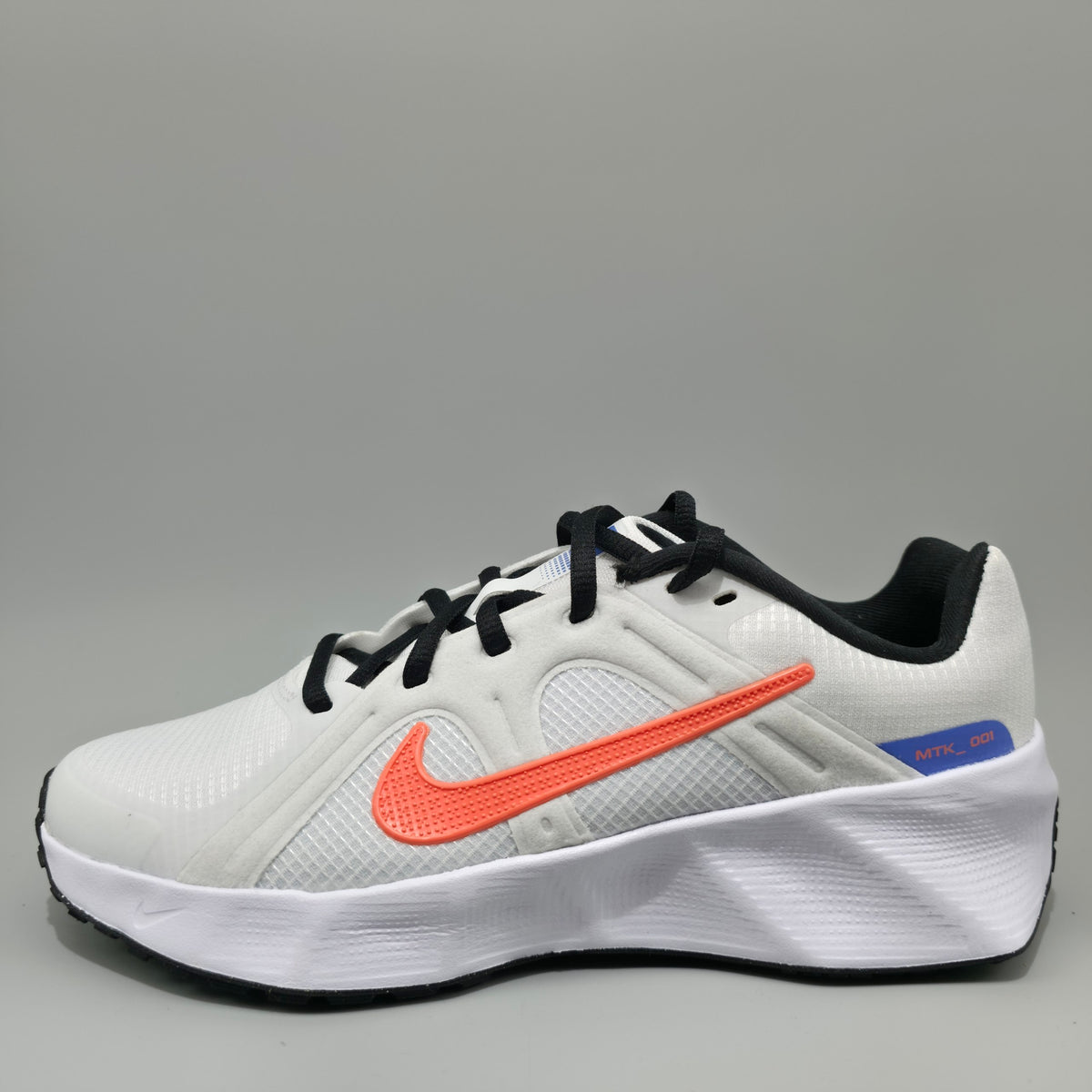 A Nike running shoe in white with a prominent orange Swoosh, black laces, and a blue and orange heel accent, photographed on a neutral gray background.