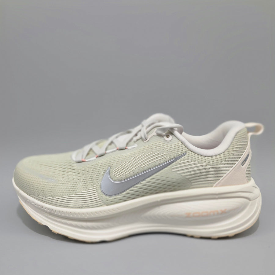 A Nike running shoe in a light sage green and white colorway, featuring a textured mesh upper, a metallic silver swoosh, and a thick white ZoomX midsole, shown against a neutral gray background.