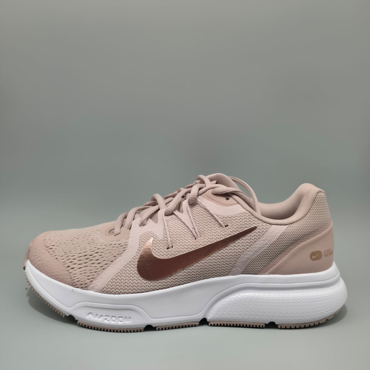 A Nike running shoe in a dusty rose pink colorway, featuring a white midsole and a metallic rose gold Swoosh on a gray background.