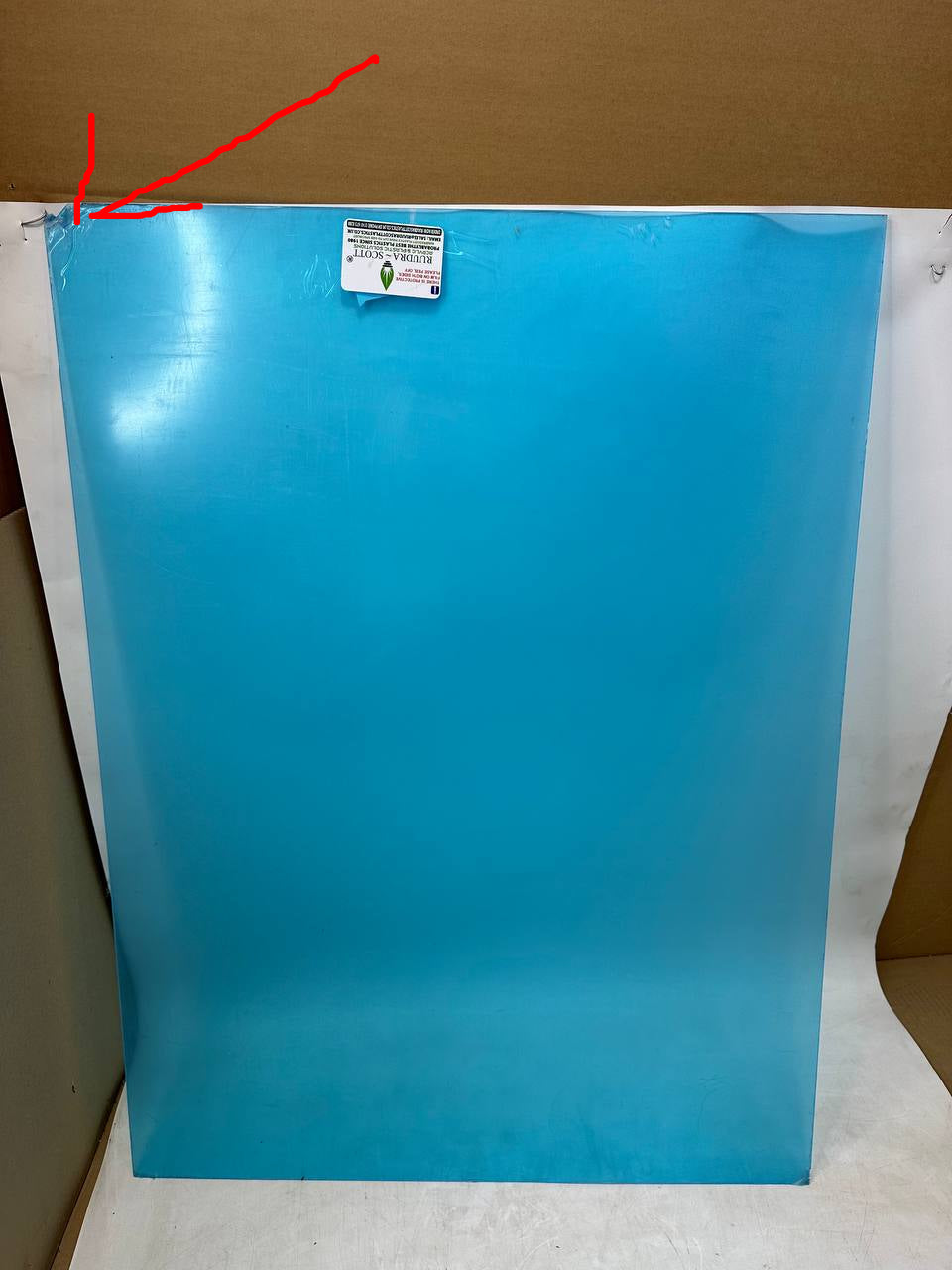 A large, solid blue rectangular sheet or panel standing vertically, secured with tape at the top, photographed against a white paper backdrop with cardboard boxes visible on the sides.