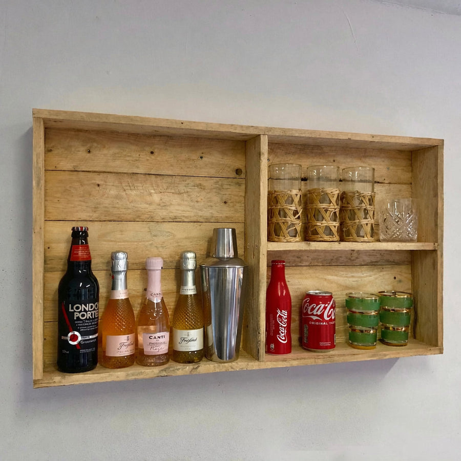 Wooden wall-mounted shelf with various bottles and glasses on a plain background