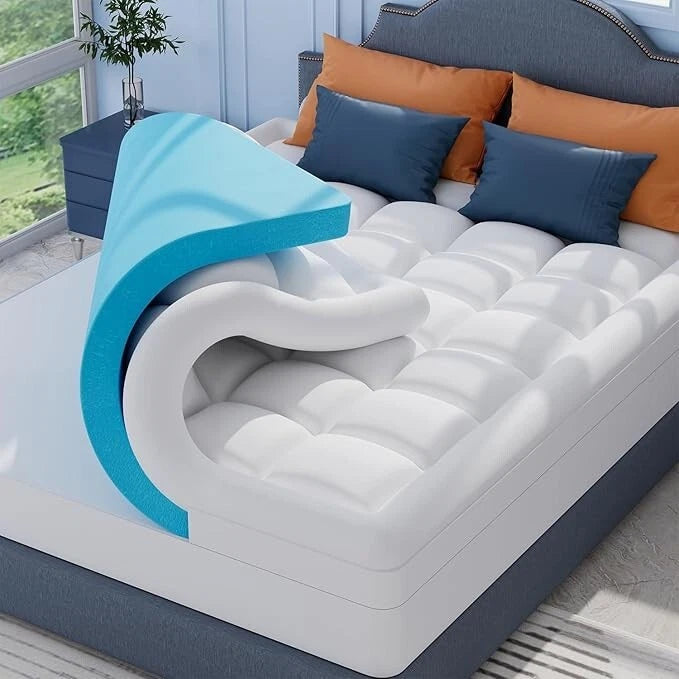 White mattress with blue foam layer on a bed with orange and blue pillows.
