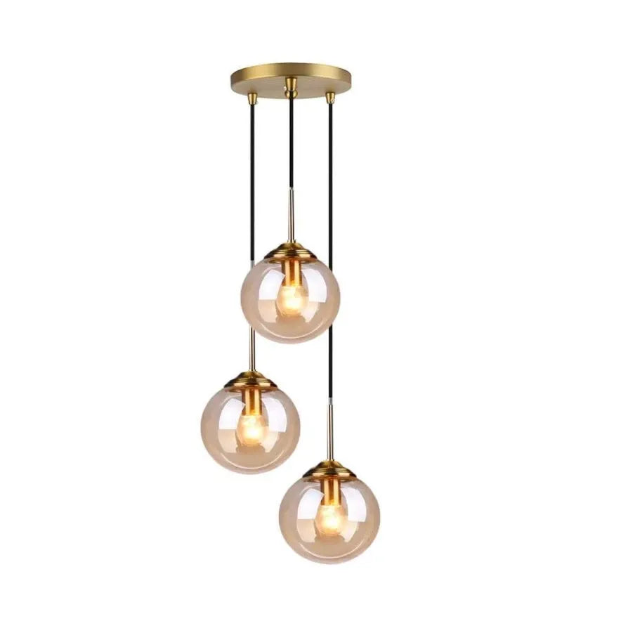 A modern three-light linear pendant chandelier with a brushed gold ceiling canopy, black hanging cords, and three clear glass shades showing warm glowing bulbs, set against a plain white background.